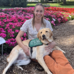 Alexis smiling sitting down on ground with yellow dog