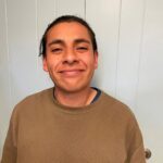 male with dark hair pulled back into a pony tail wearing a brown sweatshirt