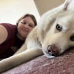 girl laying on bed by large white dog
